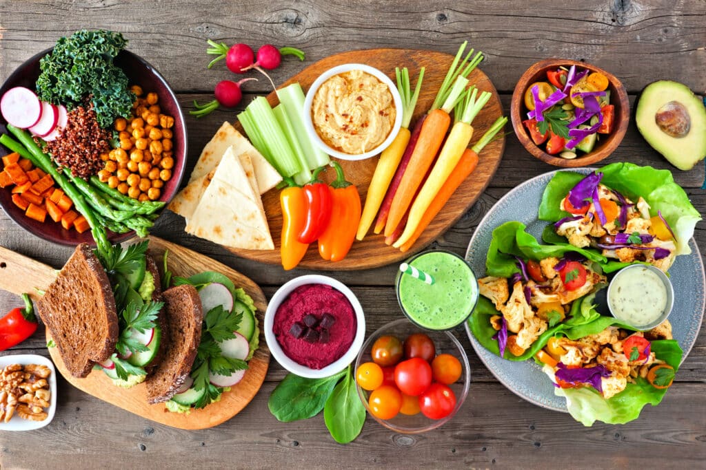 Healthy lunch table scene with nutritious Buddha bowl, vegetables, sandwiches, lettuce wraps and salad, above view over rustic wood