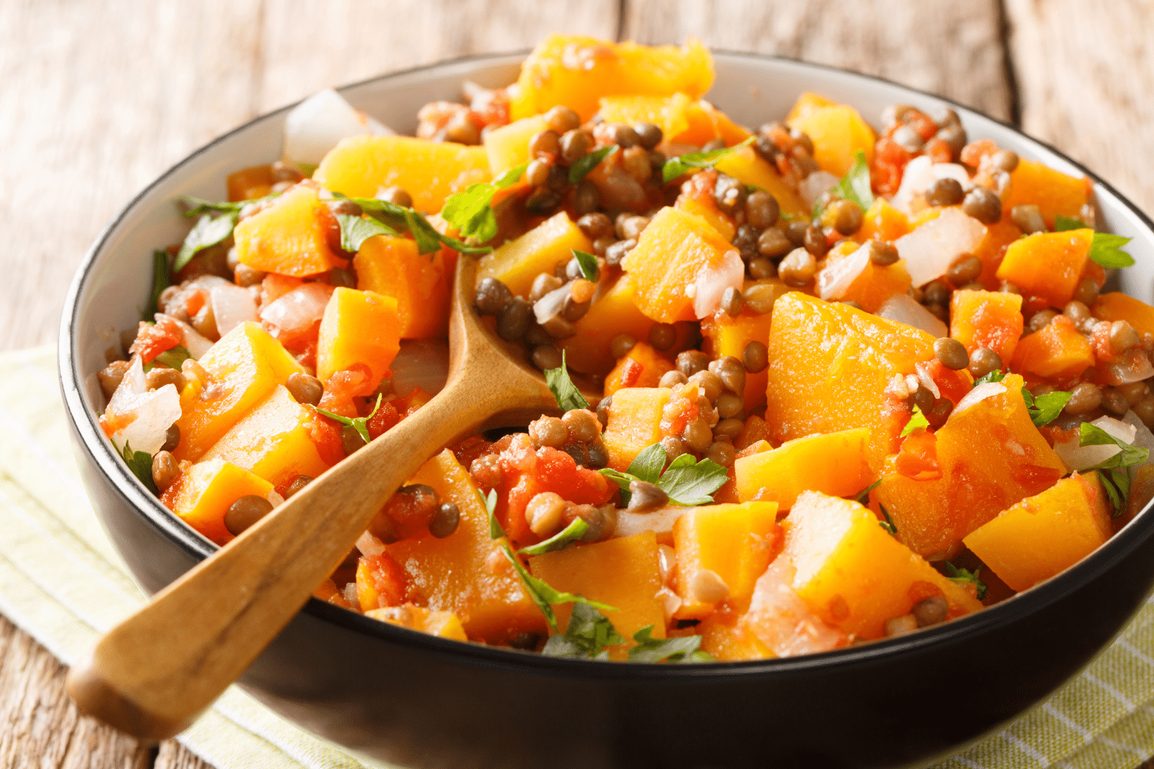 Spicy vegetable stew of pumpkins, tomatoes, lentils, onions and carrots close-up in a bowl.