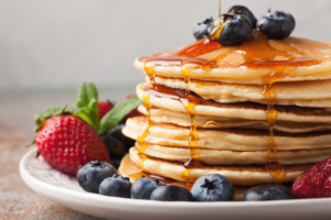 Fluffy pancakes with syrup and fruit on a plate